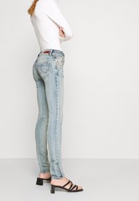 Light-wash denim jeans with a slim fit, featuring subtle whiskering, faded texture, and two back pockets. Paired with black stiletto sandals.