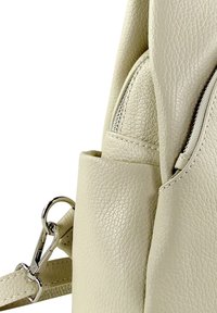 Sac à dos en similicuir beige en gros plan, présentant une surface texturée, une poche zippée et des attaches en métal argenté.