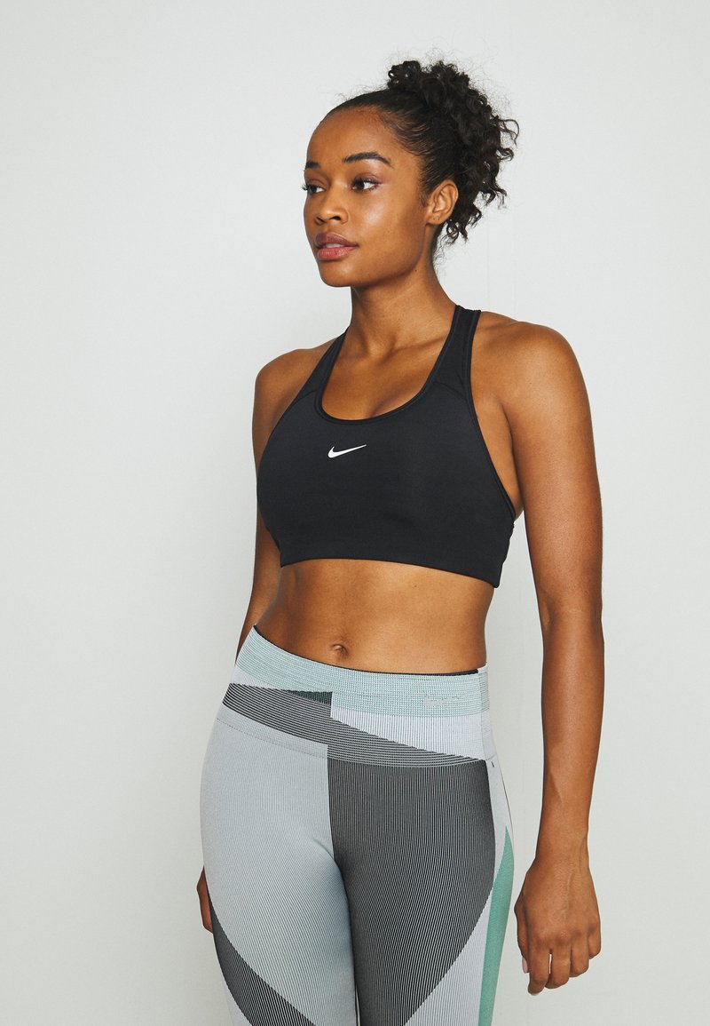 Soutien-gorge de sport noir avec un logo blanc, associé à des leggings à motifs variés présentant des teintes de gris, noir et teal dans un design rayé.