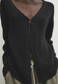Schwarzer Strickcardigan mit V-Ausschnitt und Knopfverschluss. Mit langen Ärmeln und legerer Passform, aus strukturierter Stoffqualität gefertigt.