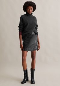 Dunkelgrauer gestrickter Rollkragenpullover, schwarze Lederwickelrock und schwarze Knöchelstiefel, vor einem neutralen Hintergrund.