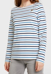 Maglietta a maniche lunghe bianca con righe orizzontali azul e blu navy, con un piccolo ornamento a forma di ape vicino allo scollo e un orlo con marchio.