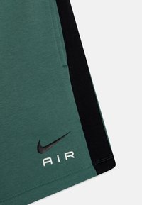 Nike šortky v zelené a černé barvě z bavlněné směsi. Obsahují boční kapsy, černé logo a bílý text "AIR". Hladká textura.