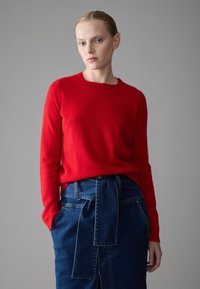 Red wool sweater with a round neckline, paired with a high-waisted denim skirt featuring a tied belt detail and side pockets.