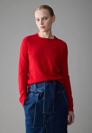 Rød ullgenser med rund hals, sammen med et høy midje denimskjørt med knytting og sidelommer.