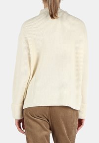 Maglione rigato color crema con collo alto, spalle cadenti e maniche lunghe. Tessuto texture e vestibilità comoda, abbinato a pantaloni in velluto a corda.