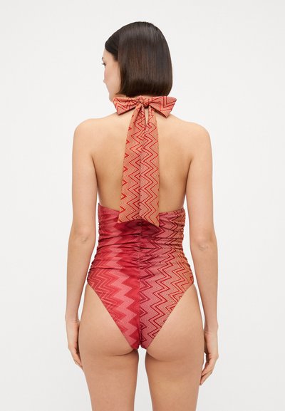Sarkans viengabala peldkostīms ar zigzaga rakstu, augstām kājām, sabīdītām malām, atvērtu aizmuguri un loku apkaklē. Gluda tekstūra.