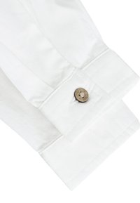 Poignet de manche de chemise blanche avec un petit bouton rond en métal gravé du mot « next » assurant le maintien du poignet.