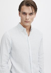 Camisa de botones azul claro y blanca a rayas. Hecha de una tela texturizada con cuello y botones en el frente. Estilizada con mangas largas.