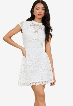 White lace dress with short sleeves, a fitted bodice, and a flared skirt. Floral appliqués adorn the neckline. Scalloped hem detail.