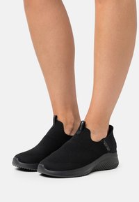 Sorte slip-on sneakers med teksturert strikket overdel og elastiske sidepaneler. Har en slitesterk gummisåle og en slank, lett design.