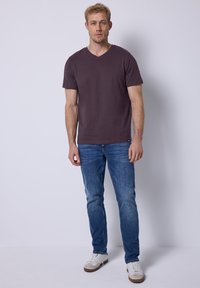 Camiseta de cuello en V de color púrpura oscuro combinada con jeans azules. El conjunto presenta un ajuste casual y zapatillas blancas con acentos beige. Estilo sencillo.