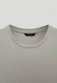 T-shirt en coton gris clair avec un col rond et des manches courtes. Texture lisse et design minimaliste. Étiquette visible à l'intérieur du col.