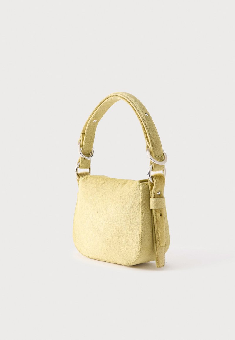 Kleine gele handtas met afgeronde onderkant, dikke verstelbare schouderriem en zilveren metalen ringen op een lichte achtergrond.