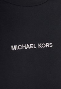 Juodas audinio viršus su apvalia kaklo linija ir raukšlėta tekstūra. Priekyje yra balta siuvinėta "MICHAEL KORS" logo.