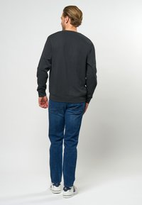 Sweatshirt griș închis cu manșete cu zimți, guler rotund și spate simplu, asortat cu blugi albaștri și adidași albi.