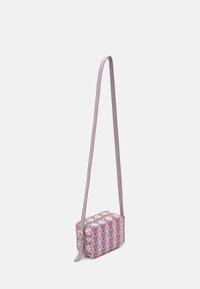 Malá obdélníková crossbody taška s dlouhým pastelově fialovým popruhem a geometrickým vzorem v růžové, červené a fialové barvě ve tvaru zigzagu.