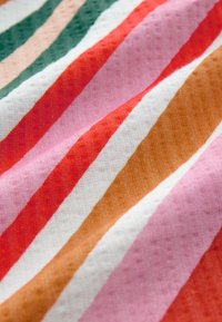 Primo piano di un tessuto morbido con righe diagonali nei colori verde, beige, rosso, rosa, bianco e marrone e un motivo testurizzato sottile.