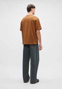 Καφέ βαμβακερό t-shirt με χαλαρή εφαρμογή, σε συνδυασμό με φαρδιά σκούρα τζιν. Μινιμαλιστικός σχεδιασμός με στρογγυλή λαιμόκοψη και κοντά μανίκια.