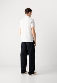 Hvid kortærmet polo-shirt parret med løstsiddende mørkeblå jeans og beige sneakers. Simpelt design uden synlige logoer eller mønstre.