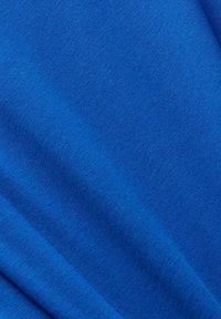Gros plan d'un tissu bleu vif et lisse avec des plis subtils et une texture fine visible.
