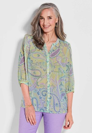 Doorzichtige blouse in lichtgroen met een paisley patroon in paars en blauw. Bevat een met knopen sluitende voorkant en driekwart mouwen met elastische manchetten.
