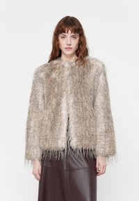 Faux fur jacket in neutral beige with a textured, shaggy appearance. Features wide sleeves and a cropped silhouette, paired with a brown skirt.