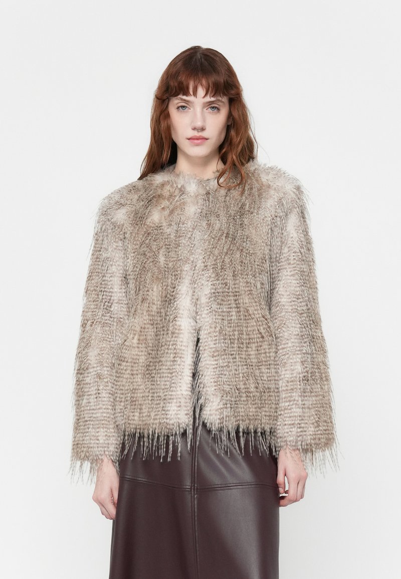 Faux fur jacket in neutral beige with a textured, shaggy appearance. Features wide sleeves and a cropped silhouette, paired with a brown skirt.