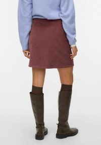 Bordeauxkleurige corduroy rok met een rechte snit, gecombineerd met kniehoge bruine leren laarzen en donkere bruine sokken. Lichtblauwe trui zichtbaar boven.