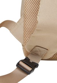 Beżowy plecak z siateczkową teksturą, regulowanym paskiem i czarną plastikową klamrą. Posiada wzmocnione szwy i lekki połysk.