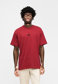 Κόκκινο βαμβακερό μπλουζάκι με κοντά μανίκια και στρογγυλή λαιμόκοψη. Διαθέτει μικρό μαύρο λογότυπο Nike στο στήθος. Ομαλή υφή, άνετη εφαρμογή.