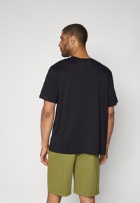 Svart bomull t-skjorte med korte ermer og rund hals, kombinert med olivengrønne shorts. Stoffet ser glatt ut, med en avslappet passform.