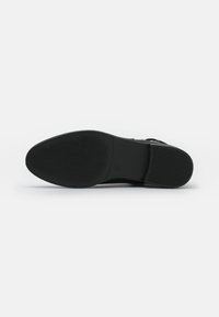 Semelle de chaussure noire avec une surface texturée. Fabriquée en matériau en caoutchouc et au design lisse, avec un talon légèrement surélevé et un logo en relief.