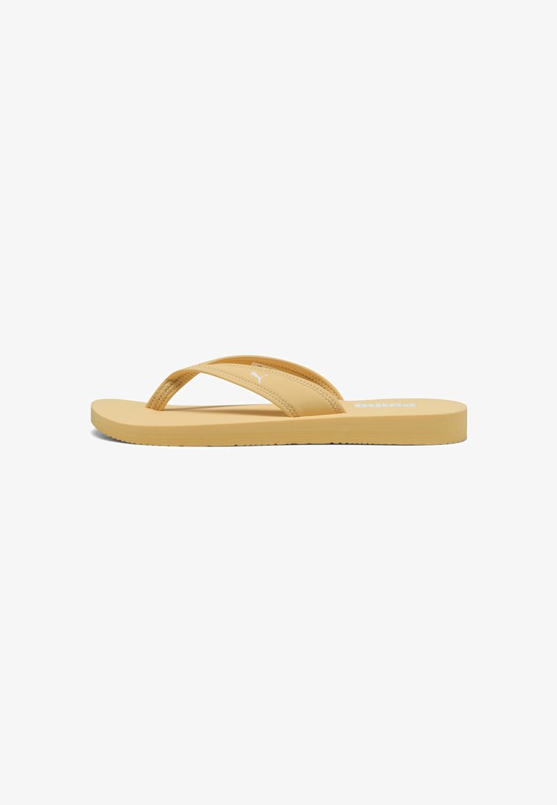 Flip-flop galben cu două curele texturate care se încrucișează peste picior, talpă plată și un mic logo pe curea superioară. Design ușor.