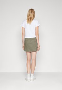 T-shirt blanc à manches courtes associé à une jupe en denim verte, dotée de deux poches arrière, portée avec des baskets blanches et des chaussettes mi-mollet.