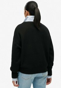 Black oversized sweater made of soft material, featuring long sleeves and ribbed cuffs. Worn over a blue and white striped collared shirt.