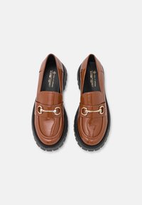 Mocassins en cuir verni brun avec une semelle noire épaisse, ornés d'une chaîne dorée sur le devant et d'un design de bout rond.