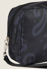 Bolsa de cosméticos negra con un patrón, textura de nailon suave, forma rectangular, cremallera plateada y correa negra detachable.