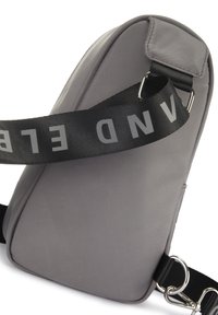 Graue Umhängetasche mit elegantem Design, aus glattem Material gefertigt, mit einem kontrastierenden schwarzen Riemen mit auffälliger weißer Schrift und metallem Zubehör.