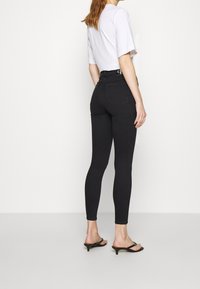 Czarne dopasowane dżinsy z denimu z wysokim stanem i tylnymi kieszeniami, zestawione z białym topem z krótkim rękawem oraz czarnymi sandałami na obcasie.