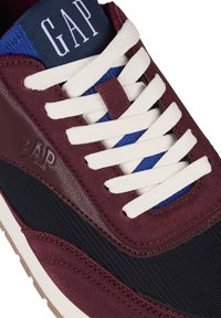 Burgundy sneaker with suede and mesh panels, white laces, navy stitching, and textured rubber sole featuring embossed logo detail.
