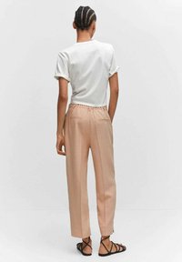 T-shirt blanc à manches courtes avec revers roulés, associé à un pantalon rose clair avec taille à cordon et poches latérales, vu de dos.