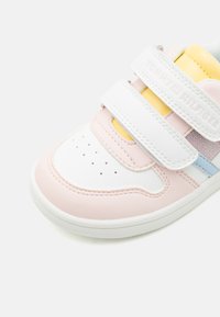 Fehér sneaker világos rózsaszín, kék és sárga részletekkel. Téglalap alakú tépőzáras pántokkal, perforált orral a szellőzés érdekében, és texturált gumitalppal rendelkezik.