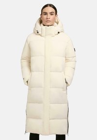 Long, cream-colored puffer coat with a hood, featuring quilted sections, side zip pockets, and a straight cut for an insulated fit.
