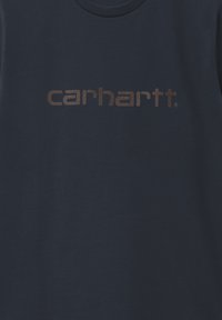 Camiseta de algodón azul marino con un gran logo de "carhartt" en color marrón y textura en el pecho. Cuello redondo clásico, tela suave.