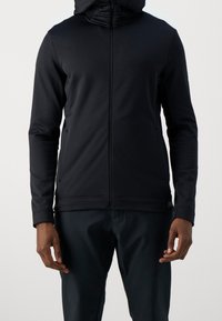 Hoodie noir zippé en tissu lisse et extensible avec une coupe ajustée. Présente un col montant et des manches amples pour le confort.