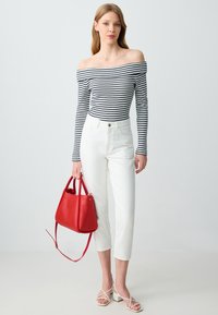 Gestreiftes Off-Shoulder-Oberteil in Marineblau und Weiß, kombiniert mit hochgeschnittenen weißen Hosen. Eine rote Handtasche und weiße Riemchensandalen runden das Outfit ab.