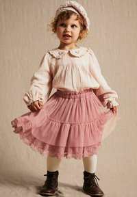Blouse texturée rose clair avec un col à volants, associée à une jupe en tulle rose à plusieurs couches avec une bordure en dentelle. Bottes en cuir marron avec lacets et collants crème.