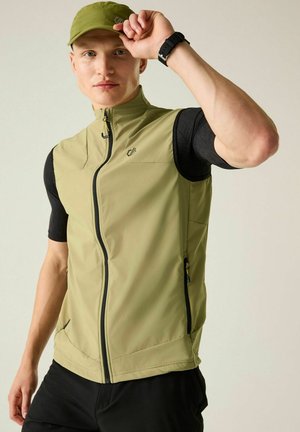 Mann trägt hellgrüne Zip-Weste und Kappe, schwarzes kurzärmeliges Shirt und schwarze Uhr, richtet mit einer Hand seine Kappe.