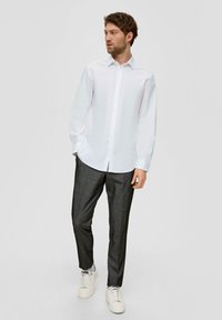 Camicia bianca a maniche lunghe con collettoButton-down, abbinata a pantaloni grigi scuri a fantasia e sneakers bianche. Design semplice e aderente.